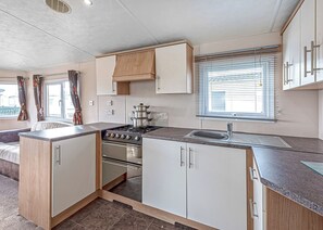 A compact kitchen with a stove, oven, and sink, wooden cabinets, and a window with blinds. - 12ft-wide quality caravan with one double and two twin. (Rhyl)
