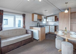 A caravan kitchen with a sofa, dining table, and cabinets. - 12ft-wide quality caravan with one double and two twin. (Rhyl)