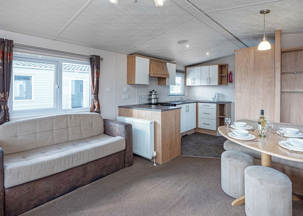 A caravan kitchen with a sofa, dining table, and cabinets. - 12ft-wide quality caravan with one double and two twin. (Rhyl)