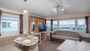 Un intérieur de camping-car compact comprenant un coin repas, un canapé, un téléviseur et une petite cuisine.