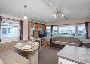 Ein kompaktes Wohnmobil-Interieur mit Essbereich, einer Sitzecke, einem Fernseher und einer Küchenzeile.