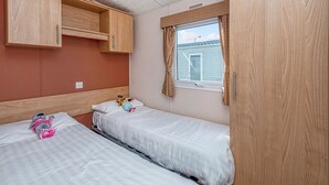 Une chambre avec deux lits, des armoires en bois, une fenêtre avec des rideaux et une vue sur une maison.