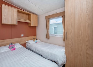 Ein Schlafzimmer mit zwei Betten, Holzschränken, einem Fenster mit Vorhängen und Blick auf ein Haus.