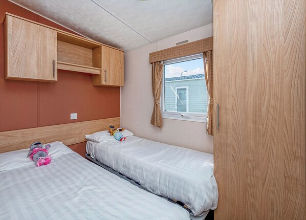 A bedroom with two beds, wooden cabinets, a window with curtains, and a view of a house.