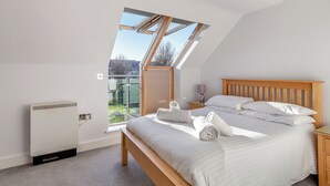 A bedroom with a skylight, a bed with white linens, a bedside table with a lamp, and a radiator.