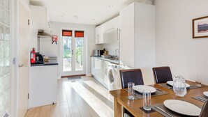 A modern kitchen with a washing machine, a dining area with a table set for two, and a view of the outdoors through a glass door.