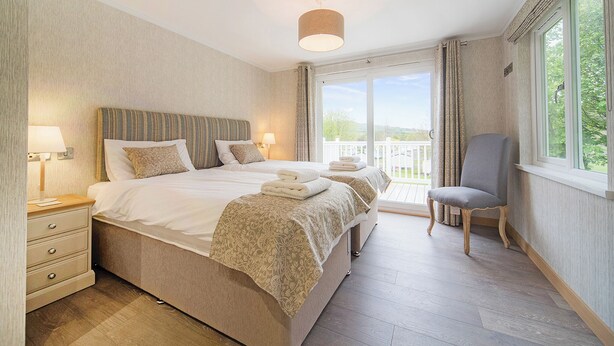 Una camera d'albergo con un letto grande, lampade ai comodini, una sedia e un balcone con vista.