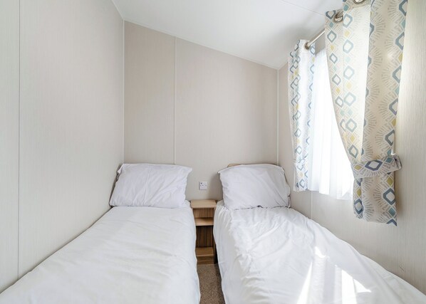 A small, single-room accommodation with two single beds, a wooden nightstand, and a curtain with a geometric pattern.
