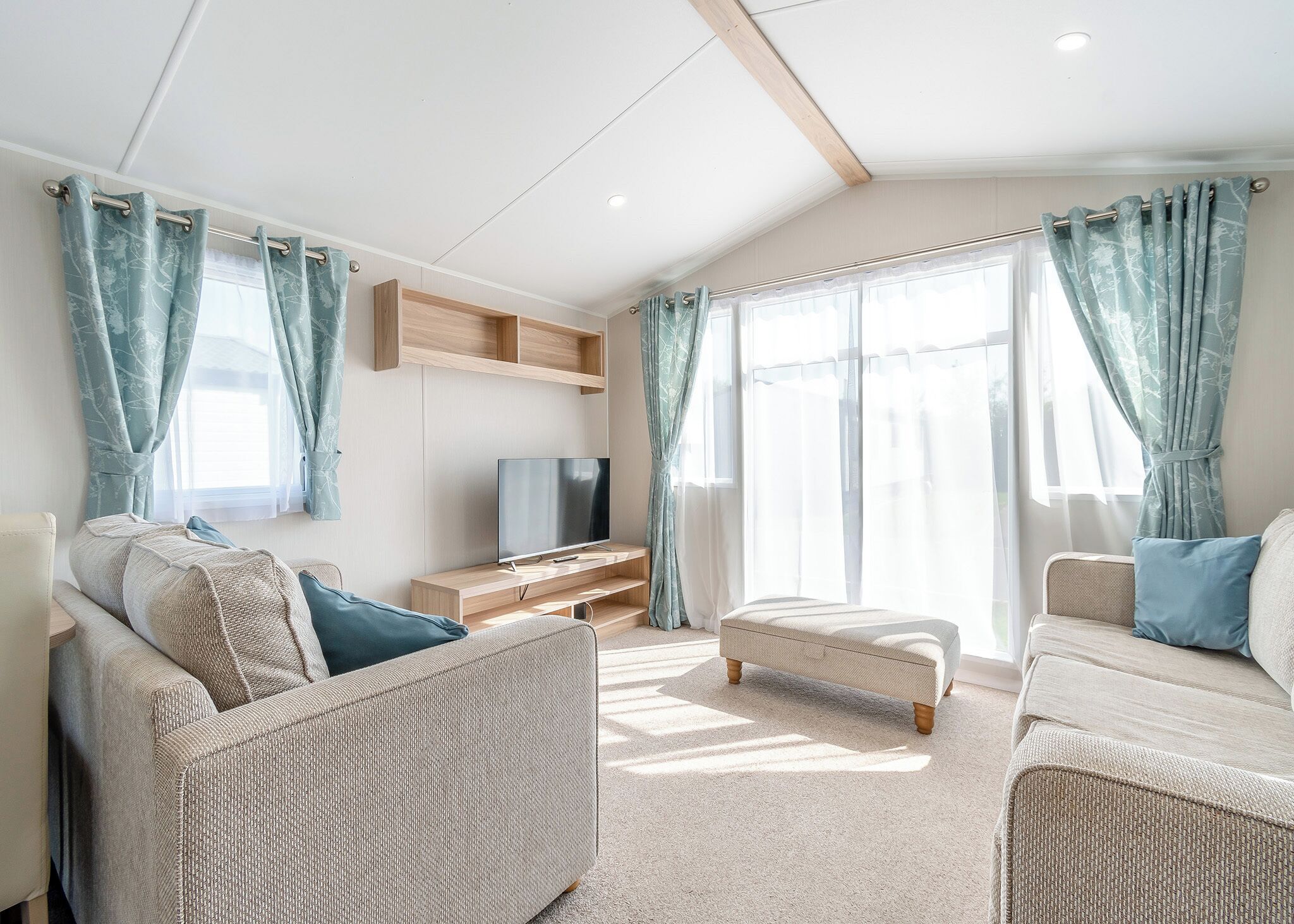 A modern living room with a flat-screen TV, wicker furniture, and large windows with curtains.