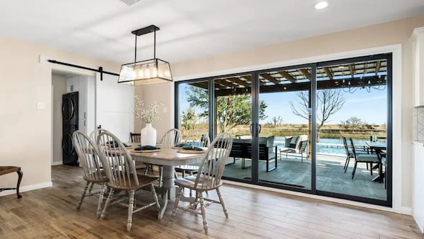 Un comedor con mesa y sillas de madera, ventanas amplias y vistas a un patio exterior con piscina.