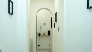 A narrow hallway with a white wall, a door on the left, and a shelf with items on the right. - Casa Pico - Centrally located with parking Wi-Fi (Mirandola)