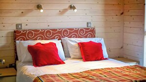 Ein Zimmer in einer Holzhütte mit einem Bett, zwei Wandleuchten und einem gemusterten Kopfteil.