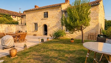 Une maison en pierre avec un patio, du mobilier d’extérieur et un petit arbre.