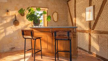 Une cuisine rustique avec un bar en bois, deux tabourets de bar, une plante en pot et un miroir suspendu.