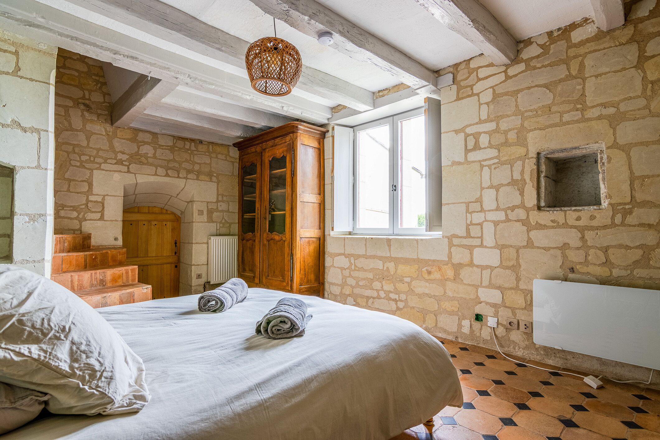 A bedroom with a stone wall, a wooden wardrobe, a window, and a radiator.