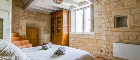 A bedroom with a stone wall, a wooden wardrobe, a window, and a radiator.