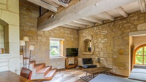 A rustic stone-walled room with a wooden dining table, a sofa, and a television.
