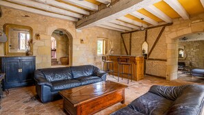 A rustic interior with stone walls, wooden beams, a leather sofa, a wooden coffee table, and a bar area.