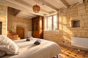 Un dormitorio con pared de piedra, un armario de madera, una cama con toallas dobladas y una ventana con vistas.