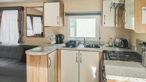 A compact kitchenette with a sink, stove, and cabinets, a window with curtains, and a sofa in the living area.