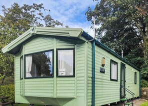 A green mobile home with a dormer window, a nameplate, and a small porch.