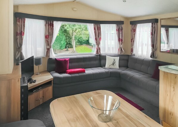 A compact living space with a sofa, a glass table, and a TV on a wooden cabinet. - 1 bedroom accommodation in Buxton (Buxton)