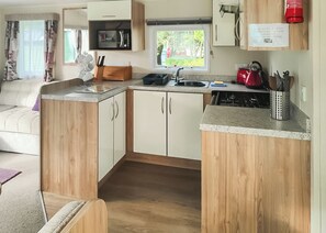 Cocina compacta con microondas, pileta y cocina. Hay un armario de madera con una encimera y una tetera roja en la encimera.