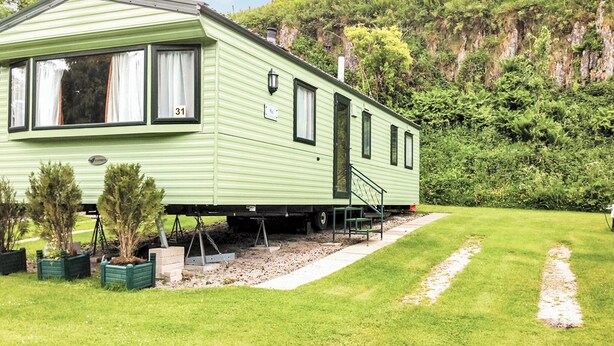 A green mobile home with a number '31' on the window, a small porch, and a grassy yard with potted plants. - 2 bedroom accommodation in Buxton (Buxton)