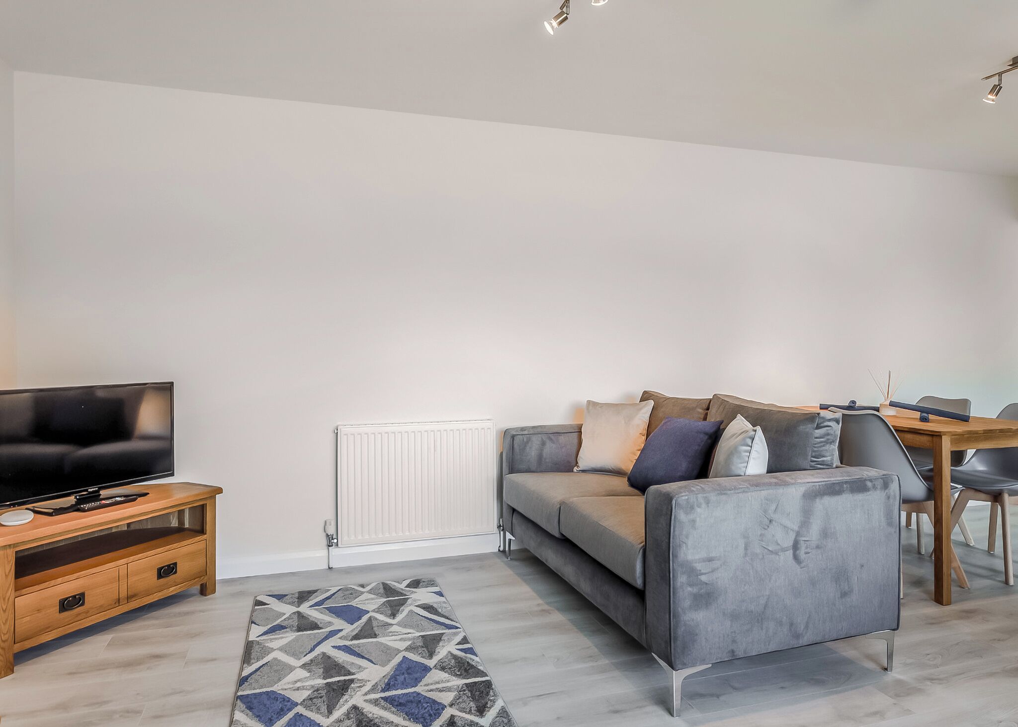 A modern living room with a sofa, a TV, a wooden side table, and a dining area with a table and chairs.
