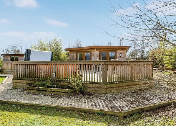 A wooden deck with a raised platform, a covered area, and a small building with windows.