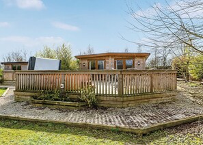 Une terrasse en bois dotée d’une plateforme surélevée, d’un espace couvert et d’un petit bâtiment avec des fenêtres.