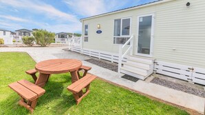 A mobile home with a picnic table and benches in the front yard.