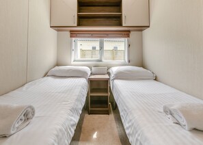 Una habitación pequeña y funcional con dos camas individuales, una ventana con persianas, un radiador y una escalera de madera.