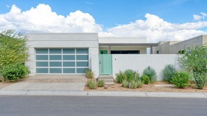 Una casa moderna de dos pisos con garaje, una puerta verde y un jardín delantero ajardinado con diversas plantas.