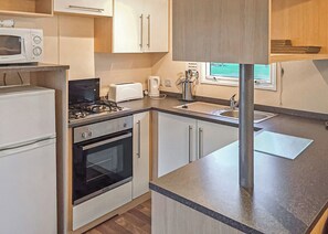 A compact kitchen with a microwave, toaster, kettle, sink, and stove.