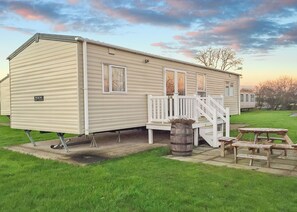 A mobile home with a porch, a small table, and a barrel.
