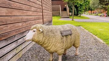 A sheep sculpture with a name tag, standing on gravel in front of a wooden building.