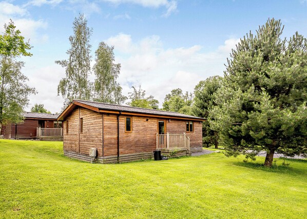 A wooden cabin with a porch, surrounded by grass and trees.