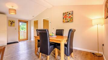 A dining area with a wooden table and four chairs, a painting on the wall, and a door leading to a balcony.