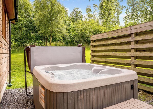 An outdoor hot tub with a wooden frame, surrounded by a wooden fence and lush greenery.