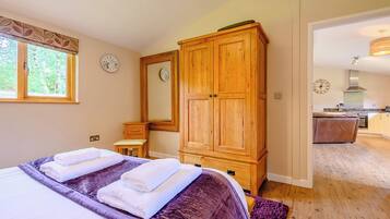 A bedroom with a bed, a wooden wardrobe, a mirror, a bedside table, and a window.