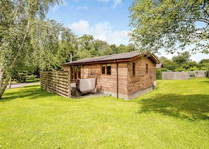 A small wooden cabin with a porch, surrounded by a grassy yard and trees.