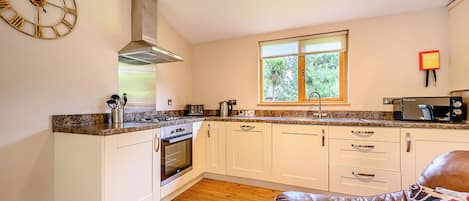 A kitchen with white cabinets, a stainless steel range hood, a window with a view, and a clock on the wall.