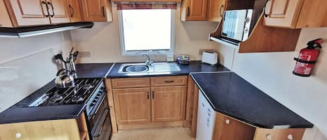 A compact kitchen with wooden cabinets, a stove, sink, and a microwave.