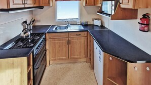 A compact kitchen with wooden cabinets, a stove, a sink, and a toaster. - Excellent Value for money Bronze range, with one double bedroom and one twin. (Clarach Bay, Nr Aberystwyth)