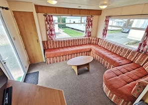 L’intérieur d’une caravane est aménagé avec un canapé incurvé, une petite table ronde et une porte donnant sur l’extérieur.