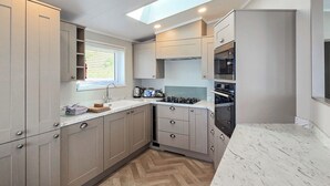 A modern kitchen with built-in appliances, a herringbone wood floor, and a skylight.