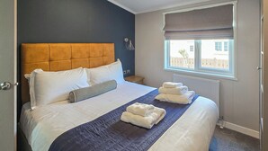 A hotel room with a large bed, a headboard, a window with a view, and a bedside table.