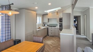 A compact kitchen with modern appliances, a dining area with a wooden table, and a hallway leading to other rooms.