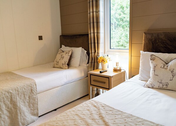 A bedroom with two single beds, a nightstand with a lamp, and a window with curtains.